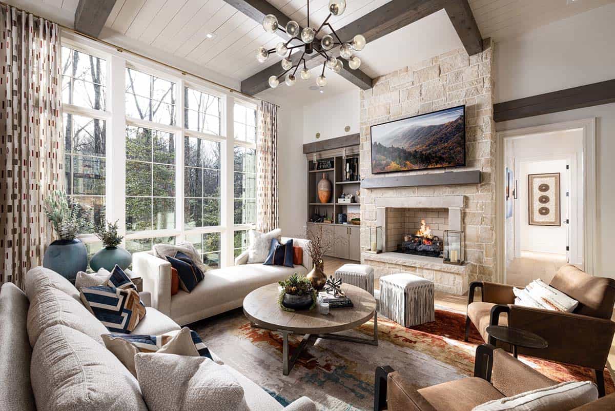 Living room with stone fireplace, exposed beams, sputnik chandelier, and large windows