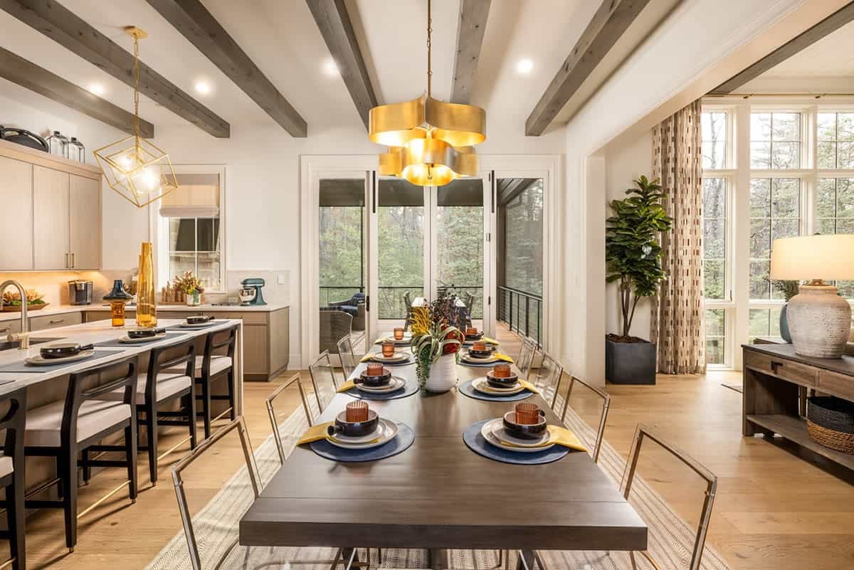 Open-plan dining room with gold chandelier, dark wood table, and forest views