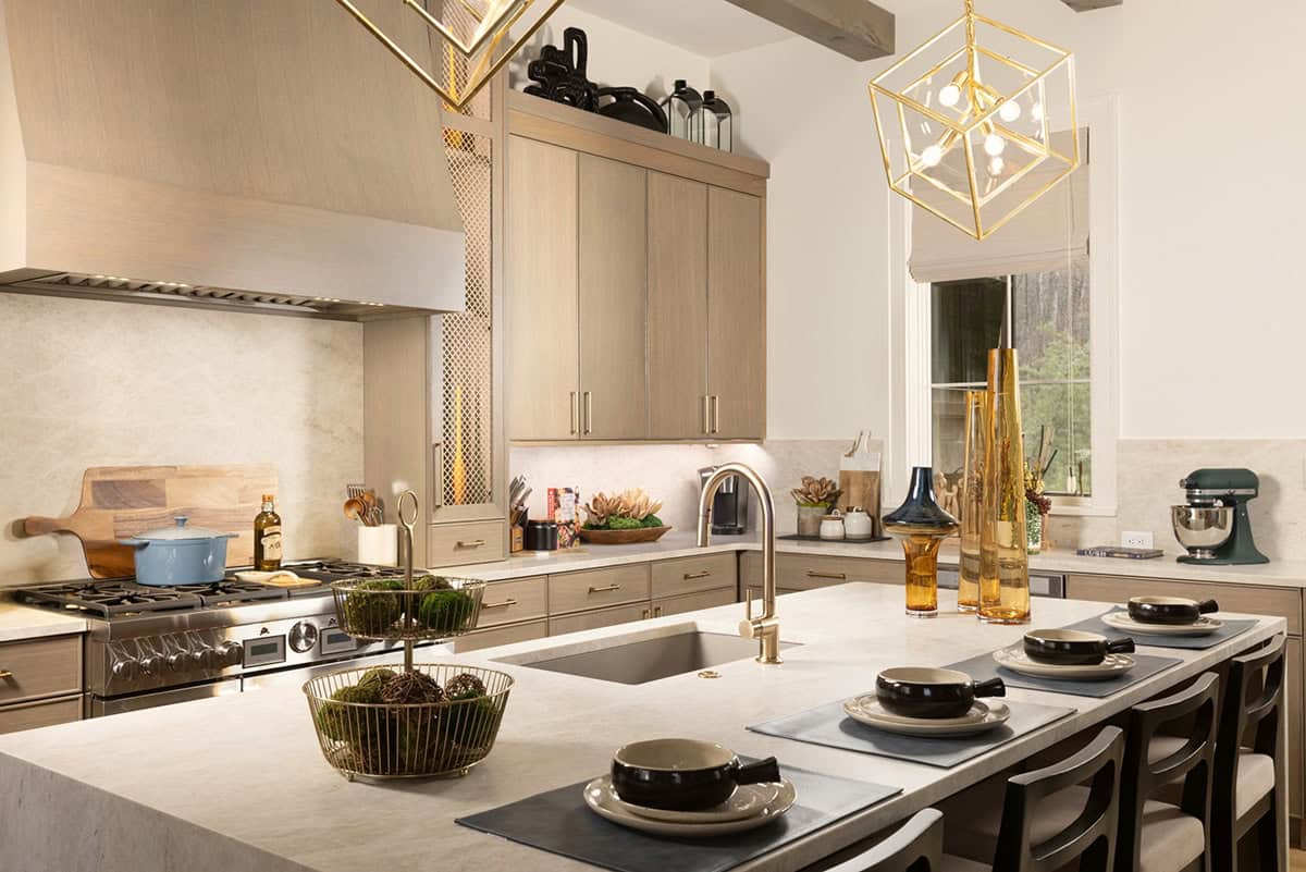 Kitchen with taupe flat-front cabinets, quartz island, gold cube pendants, and pro range