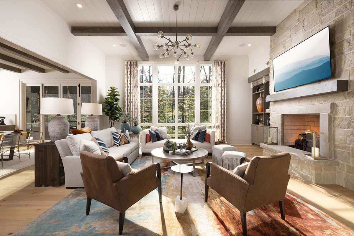 Bright great room with exposed beams, stone fireplace, and colorful area rug