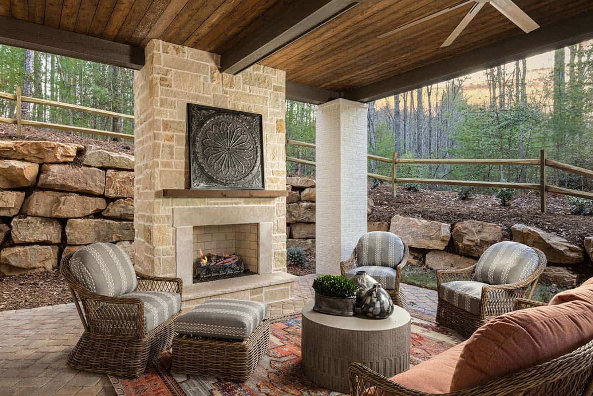 Lower covered patio with limestone fireplace, wicker seating, and wooded views