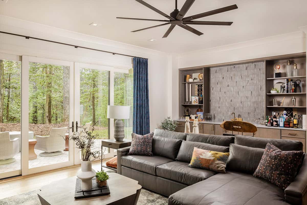 Lower-level family room with leather sectional, built-in bar, and forest-facing glass doors