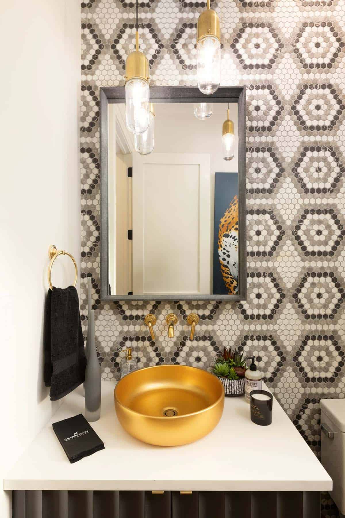 Powder room with mosaic hex tile wall, gold vessel sink, and brass pendant lights