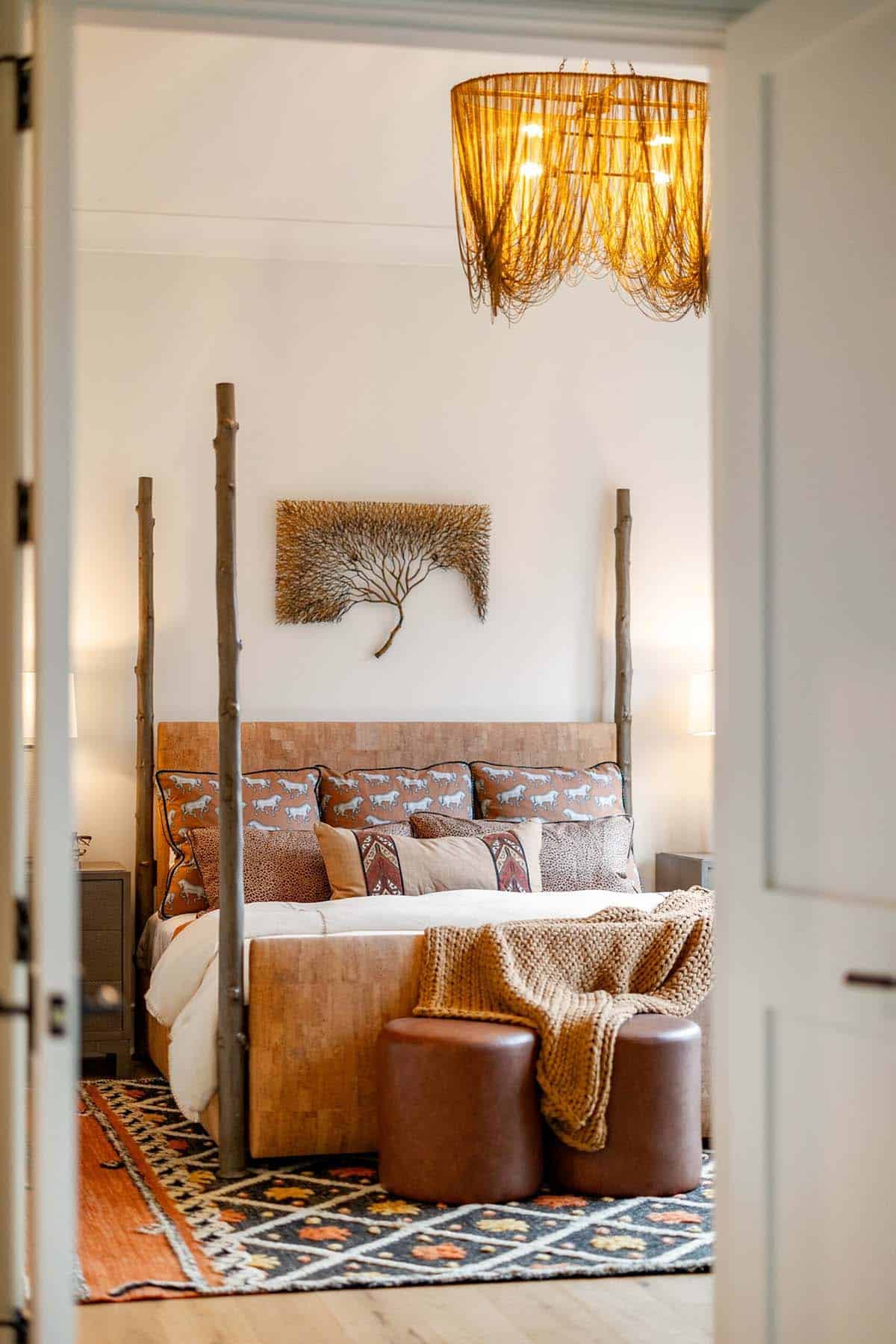 Doorway view into primary bedroom with branch four-poster bed and woven rattan chandelier