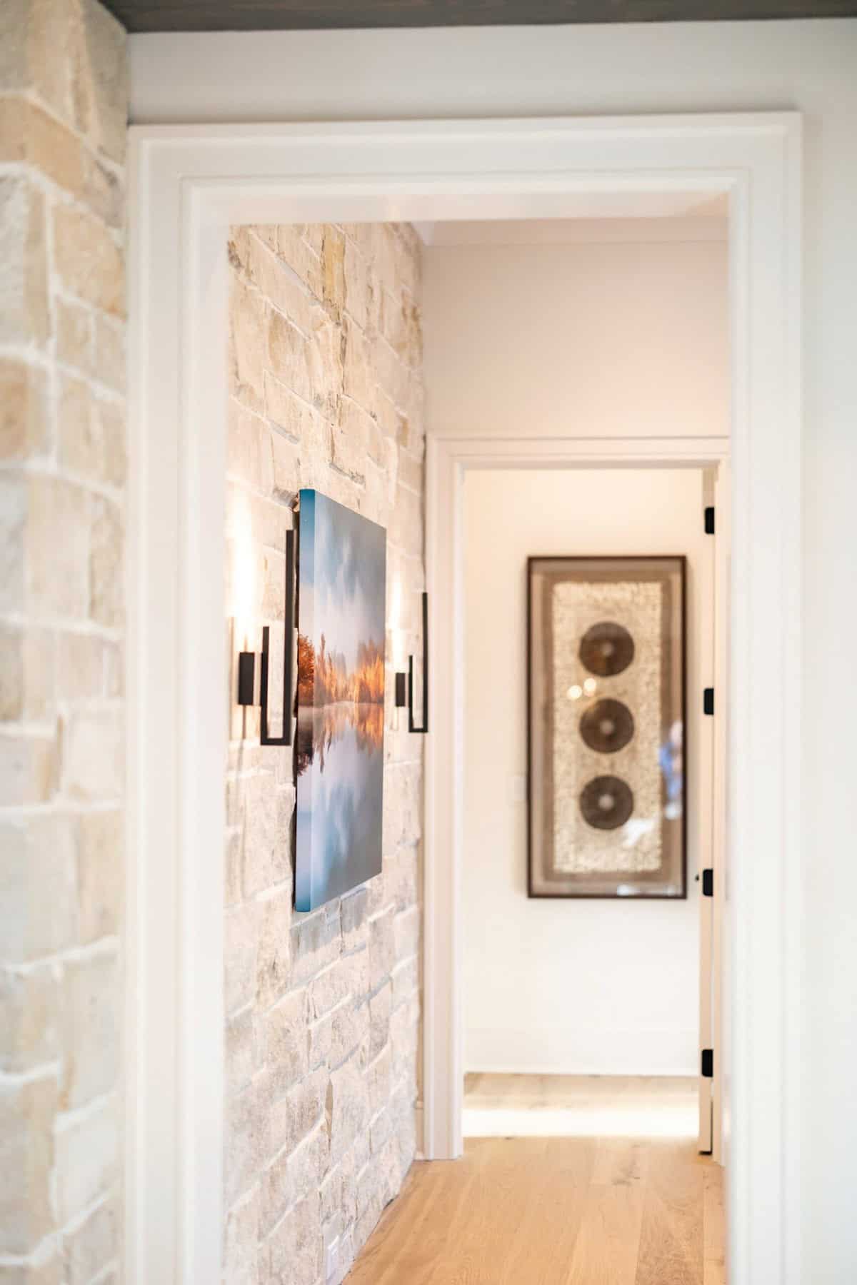 Hallway with limestone accent wall, black sconces, and landscape art