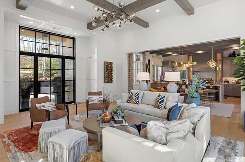 Open-concept living room with gray exposed beams, sputnik chandelier, cream sofas, and steel-framed glass doors