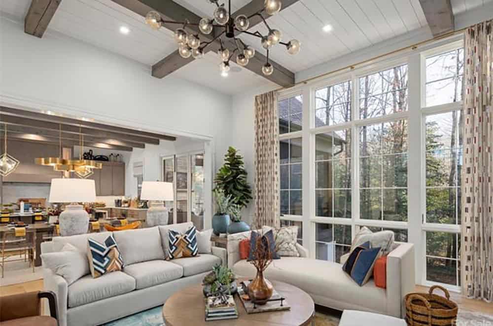 Living room with vaulted beamed ceiling, sputnik chandelier, neutral sofas with blue and orange pillows, and floor-to-ceiling windows
