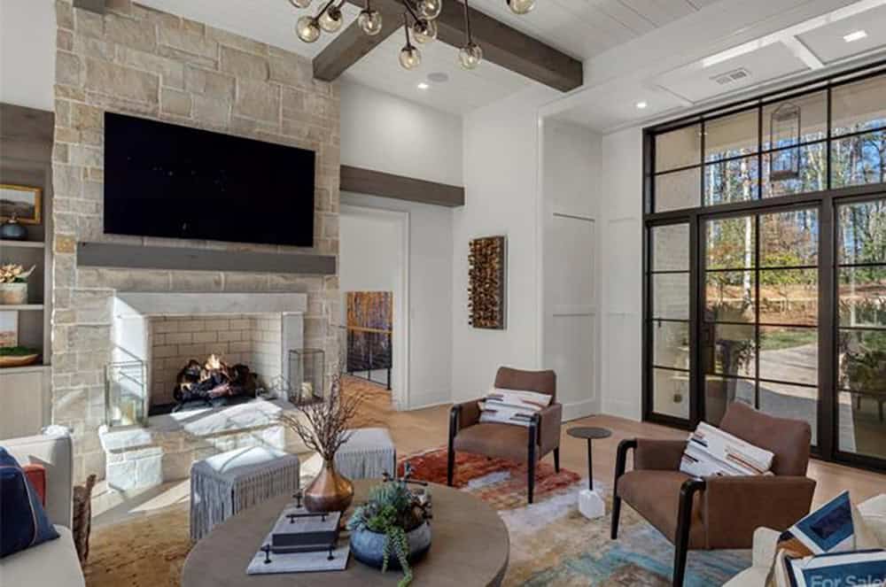 Living room featuring floor-to-ceiling stone fireplace with TV, exposed beams, and steel-framed glass entry doors