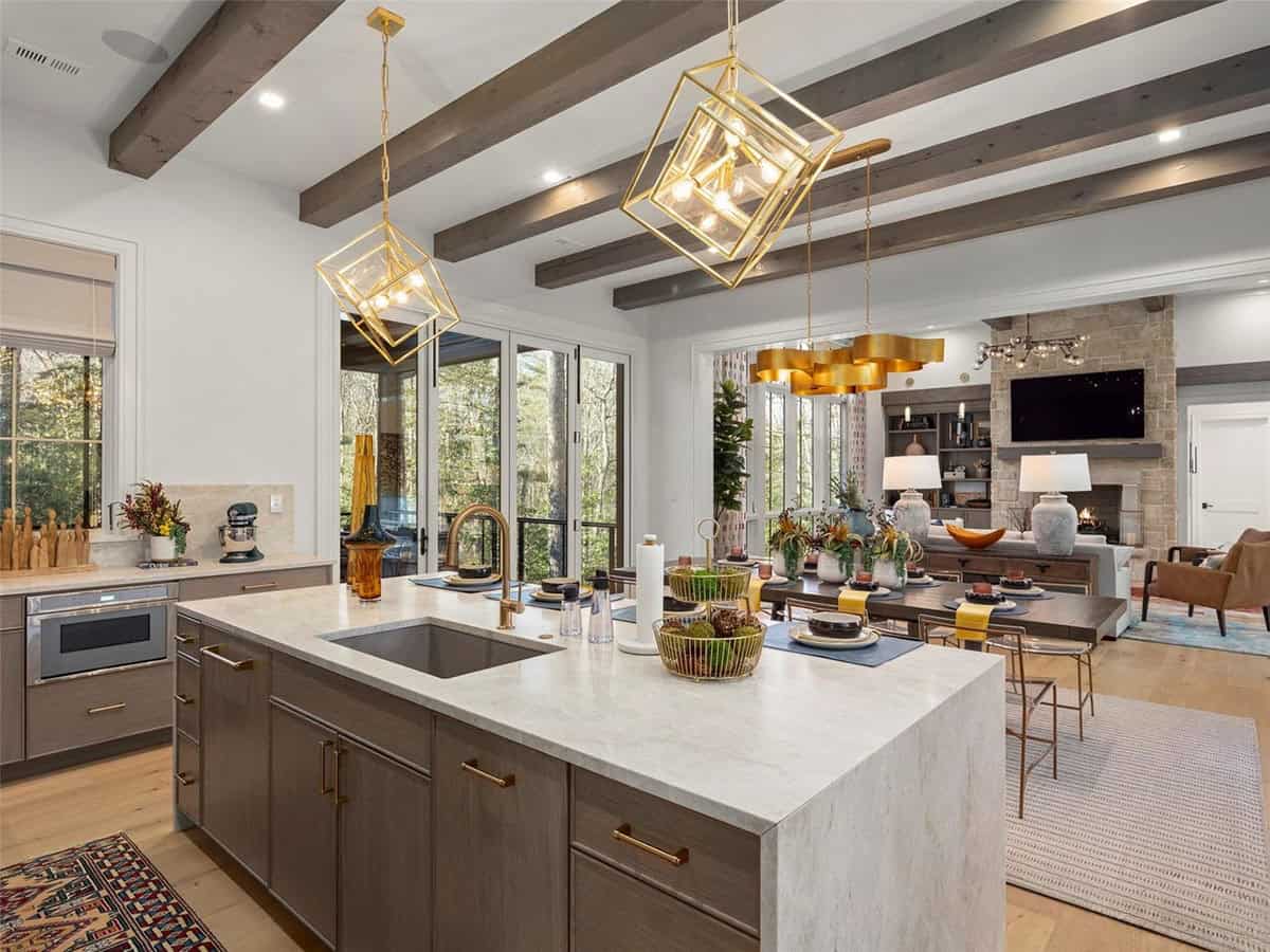Large kitchen island with stone countertop, gold cube pendants, gray cabinetry, and views to living and dining areas