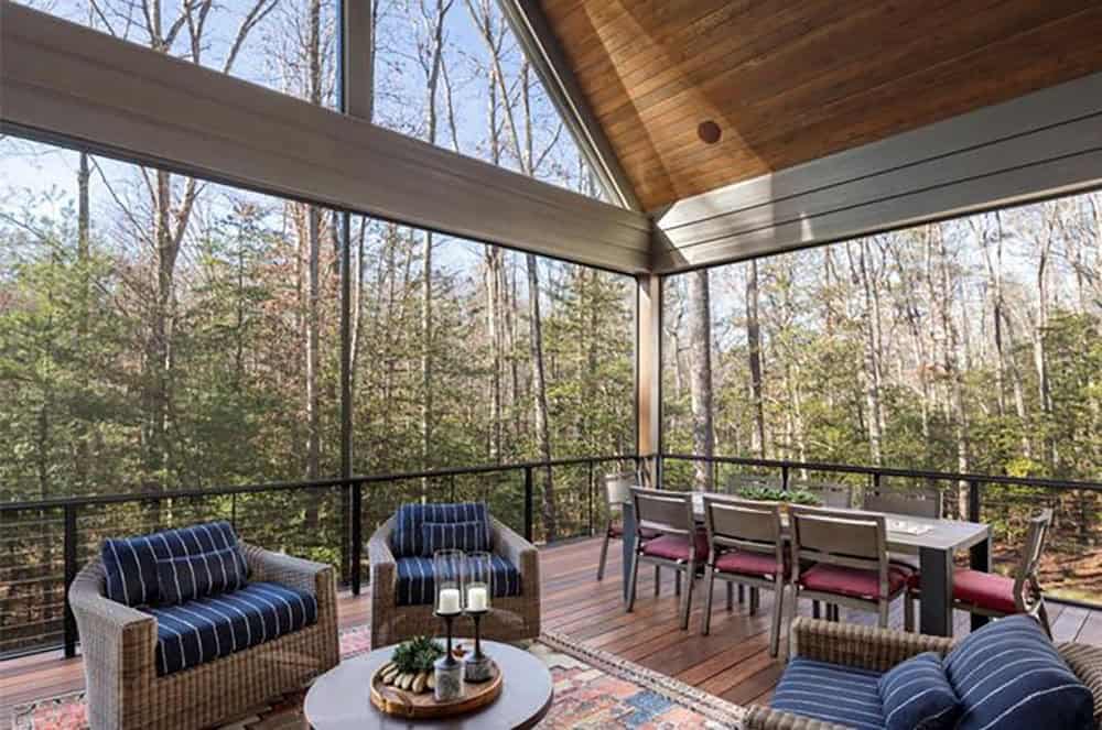 Screened porch with cathedral wood ceiling, panoramic wooded views, wicker seating, and cable rail deck