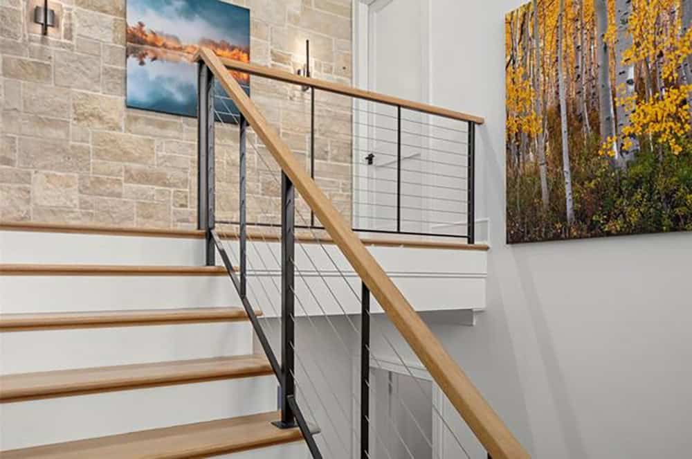 Modern staircase with light oak treads, black steel cable railing, and stone accent wall