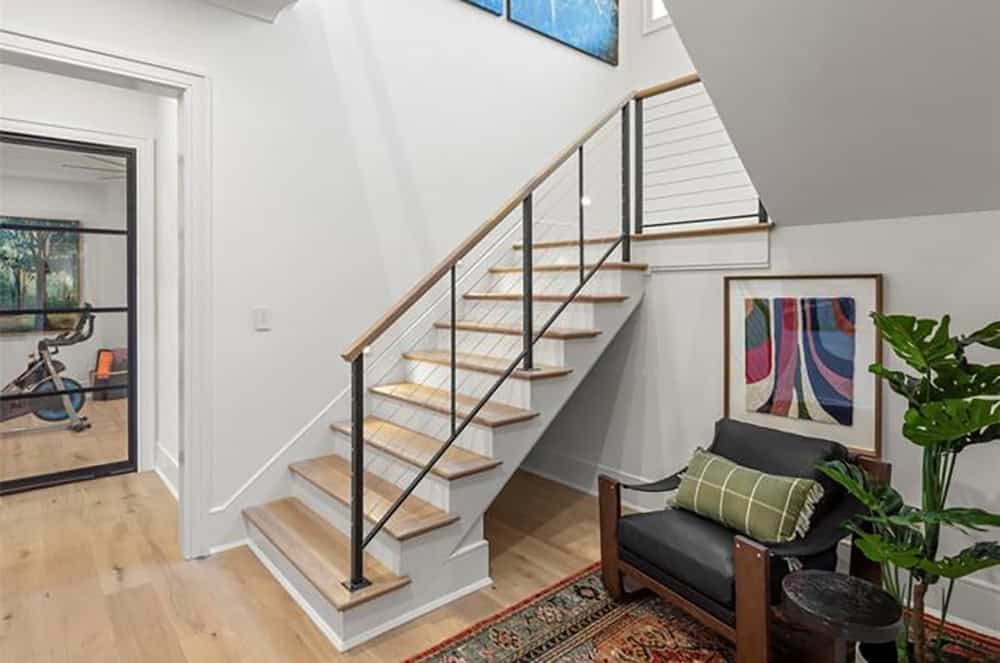Staircase with oak treads and cable railing, adjacent home gym with steel-framed glass door