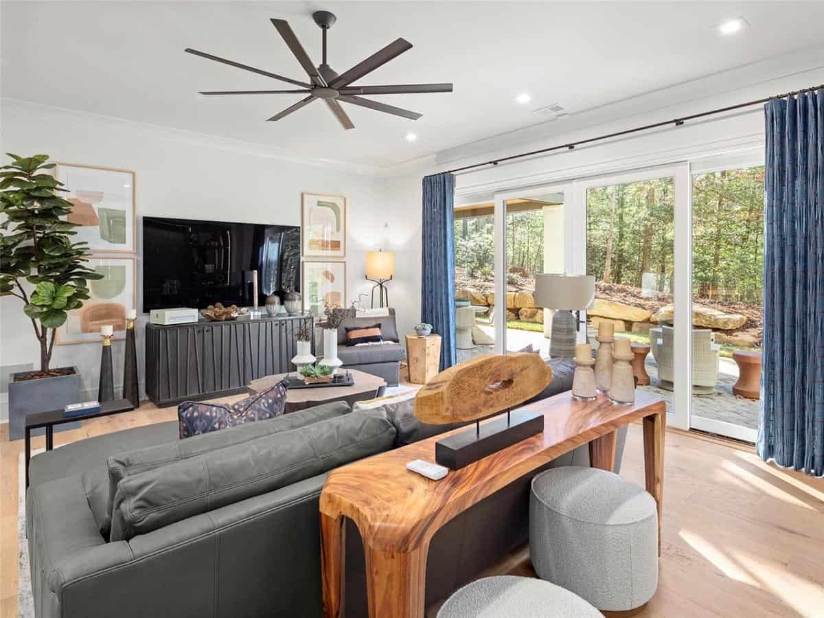 Lower-level family room with leather sectional, live-edge console table, large ceiling fan, and patio access