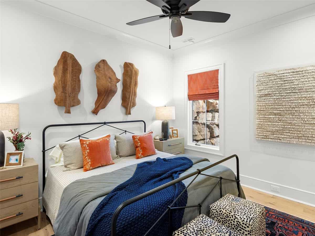 Guest bedroom with black iron bed frame, carved wood leaf wall art, orange accent pillows, and navy knit throw