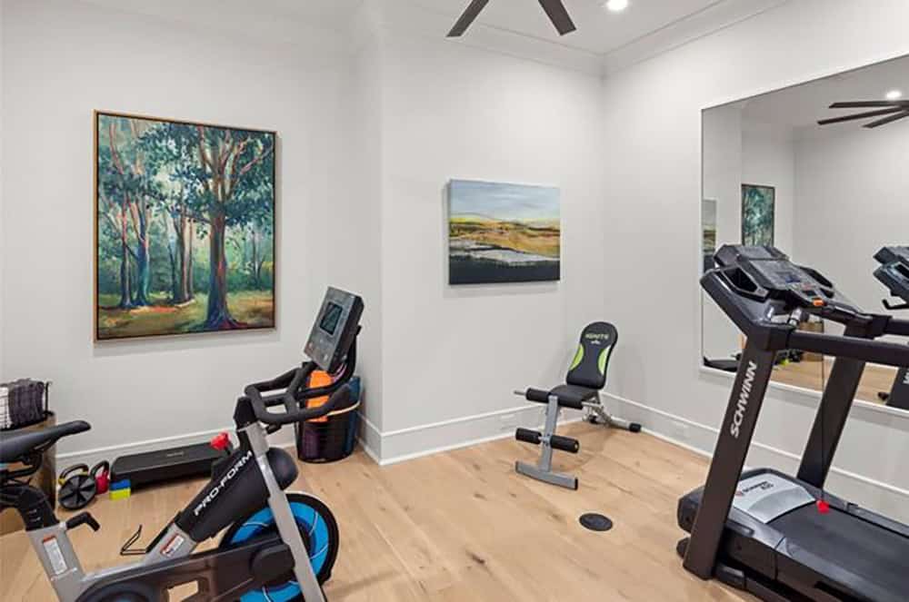 Home gym with spin bike, treadmill, floor-to-ceiling mirror, and landscape paintings on white walls