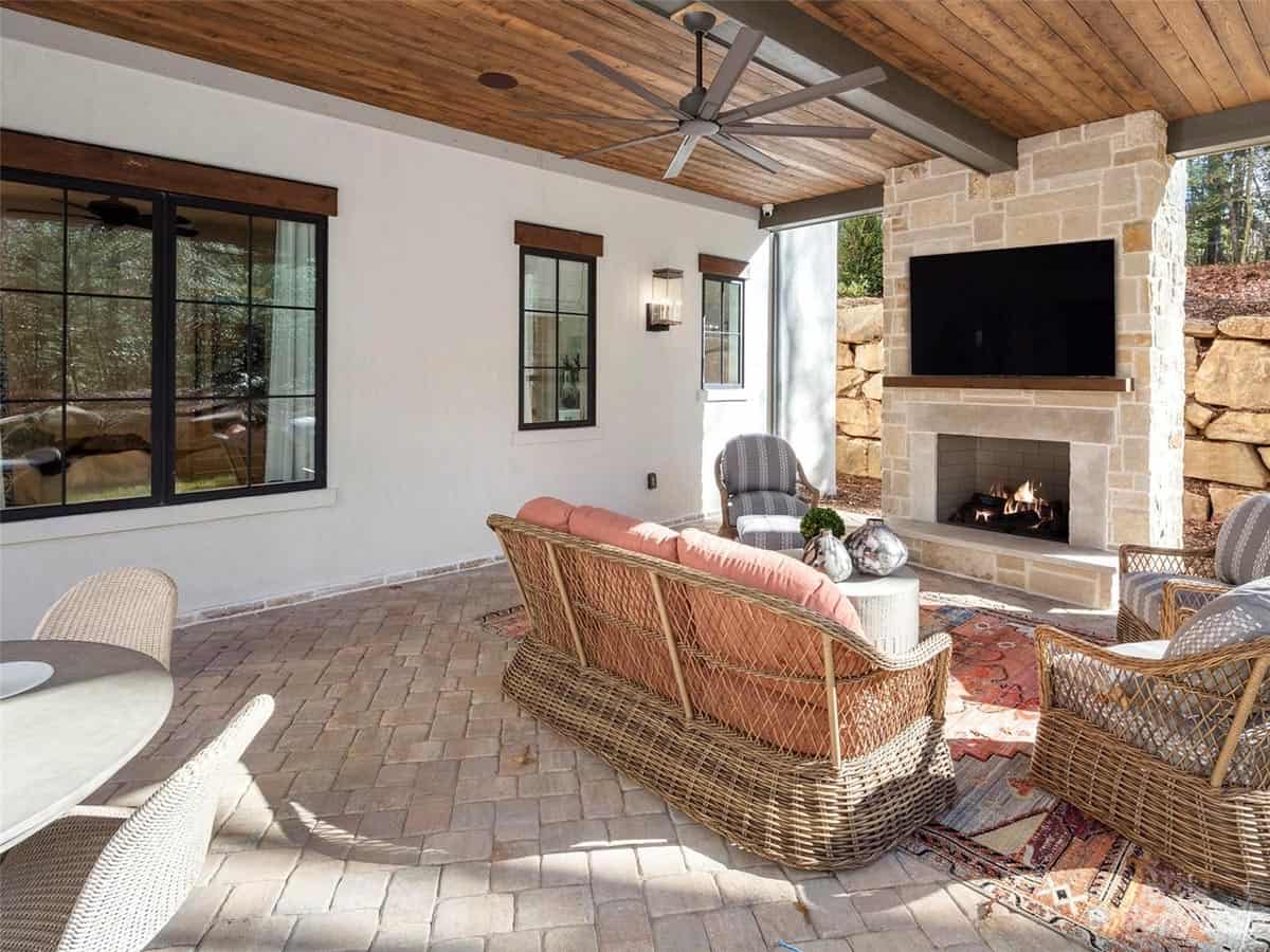 Covered patio with wood ceiling, oversized ceiling fan, wicker sofa with coral cushions, and stone fireplace with TV
