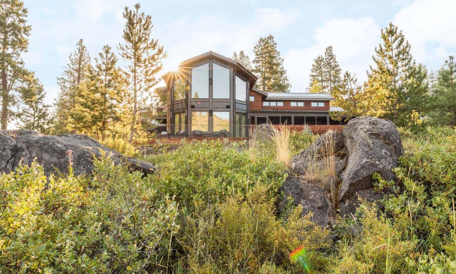 Exterior of a contemporary wood and glass home seen through native shrubs and boulders at golden hour