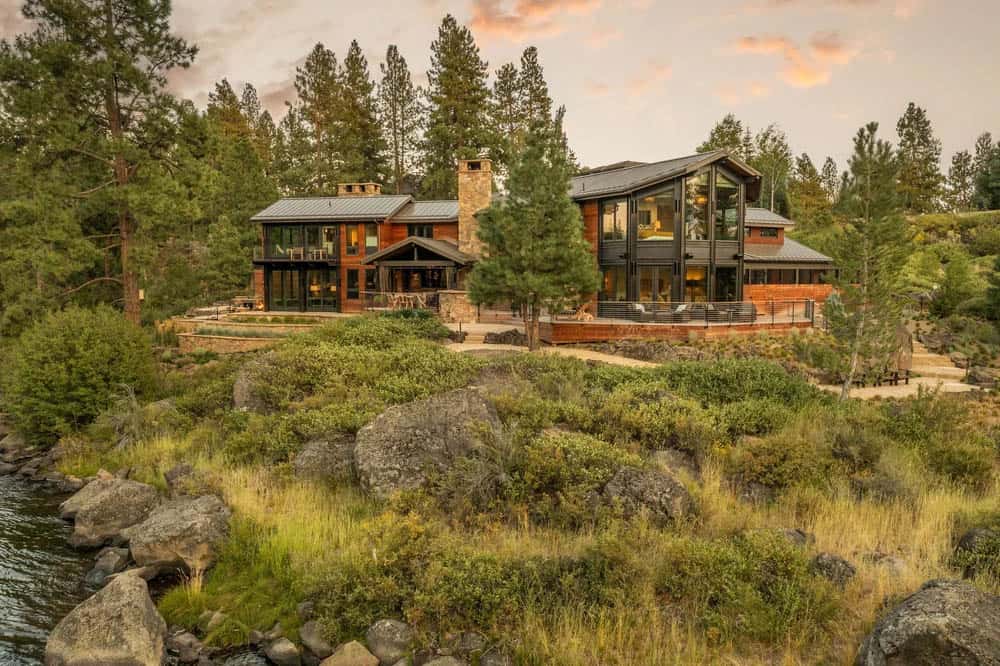 Full exterior view of a multi-generational river retreat with two connected structures at sunset
