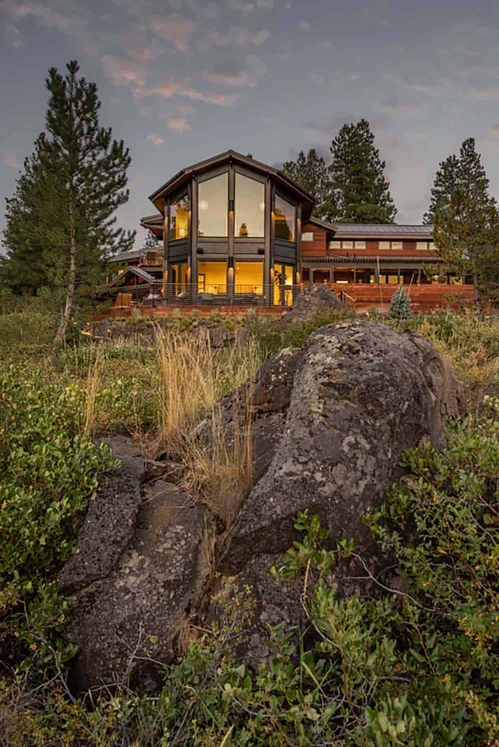 Low-angle dusk view of a contemporary glass and cedar home rising above rocky terrain and native vegetation
