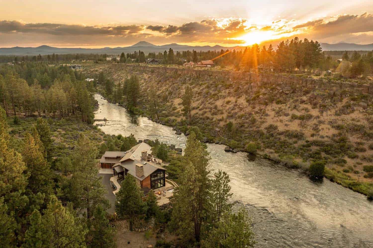 Wide aerial shot of a riverside retreat along a winding Oregon river canyon at golden sunset
