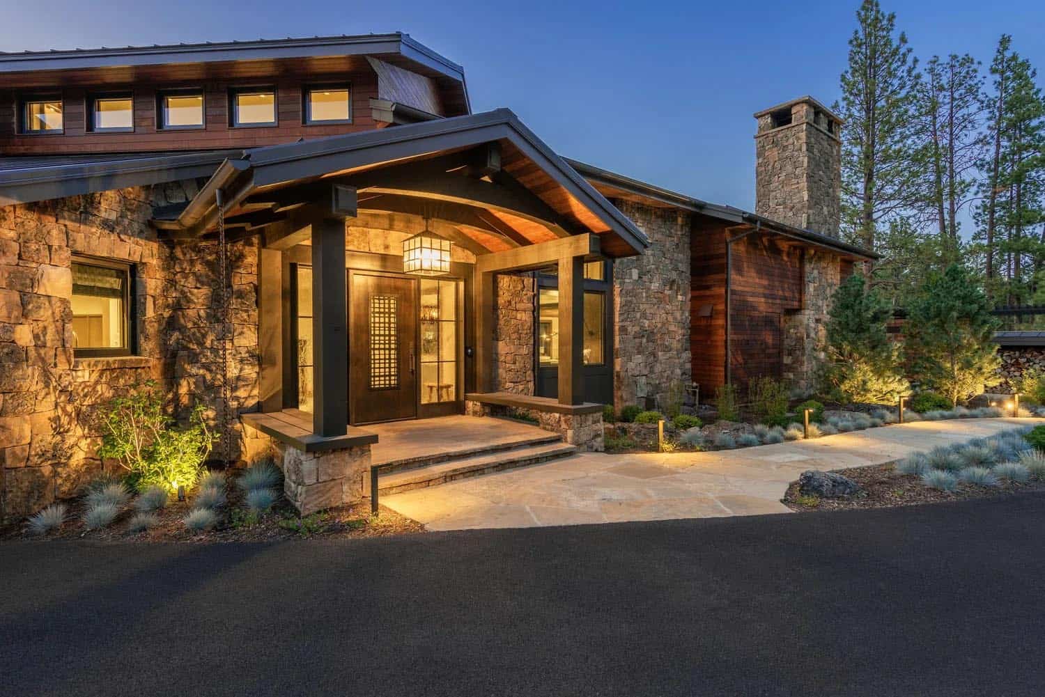 Illuminated front entry of a stone and wood craftsman-style home at twilight with lantern lighting