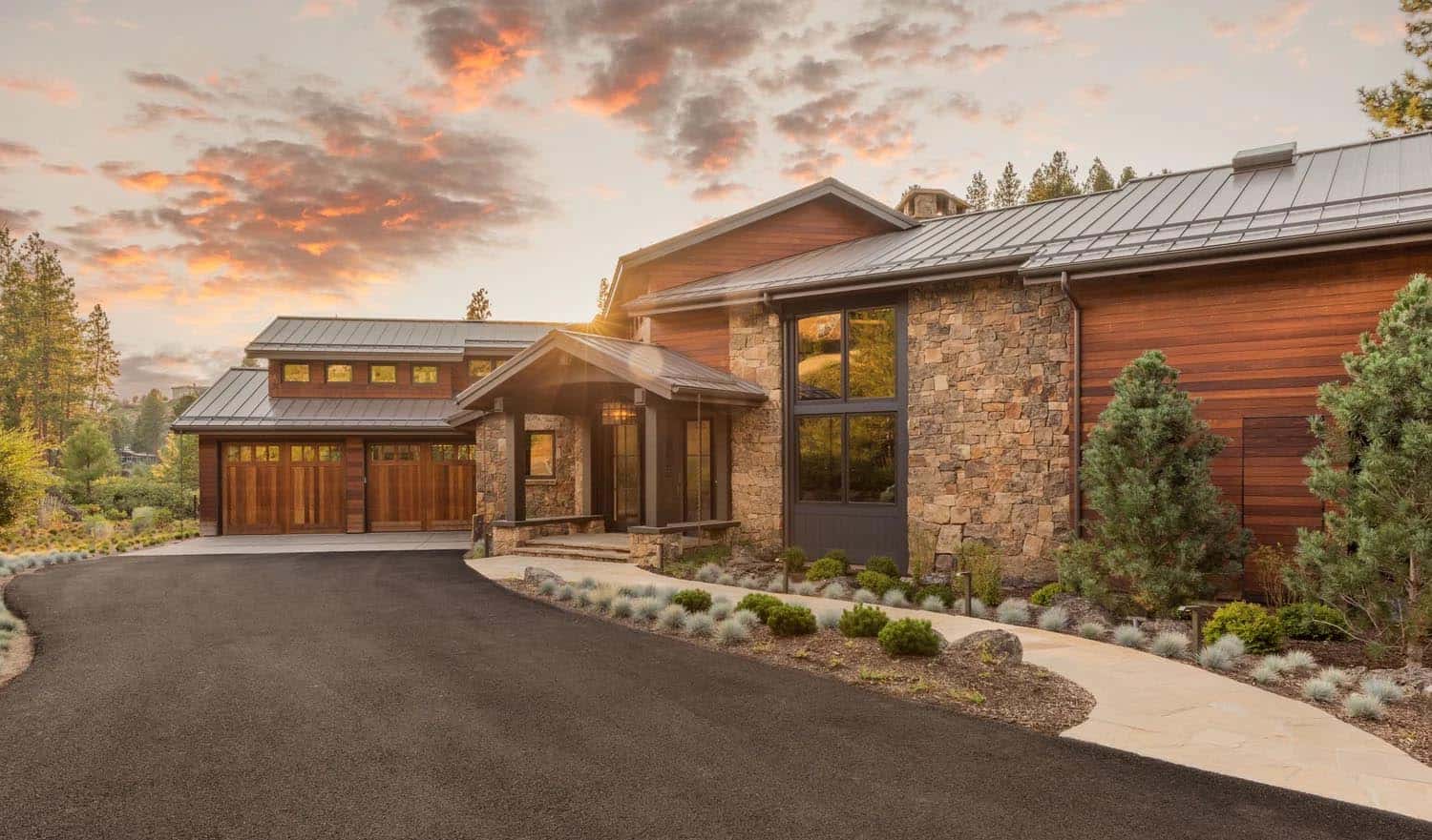 Street-facing exterior of a multi-wing cedar and stone home with metal roof at sunset