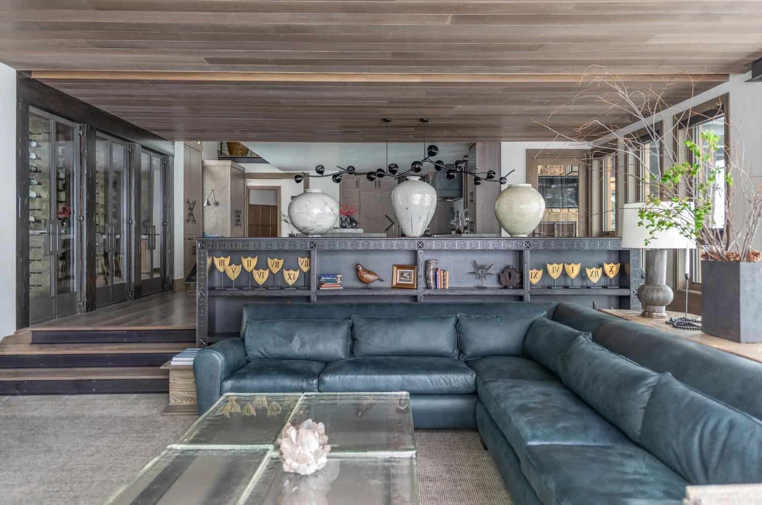 Interior living room with a large navy leather sectional, decorative metal shelving, and glass wine room beyond