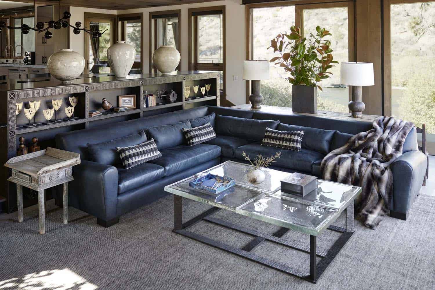 Sunlit living room featuring a navy leather sectional, glass coffee table, and river views through large windows