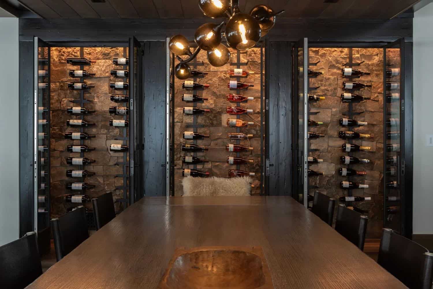 Interior wine room with floor-to-ceiling bottle racks on stone walls and a long wooden dining table