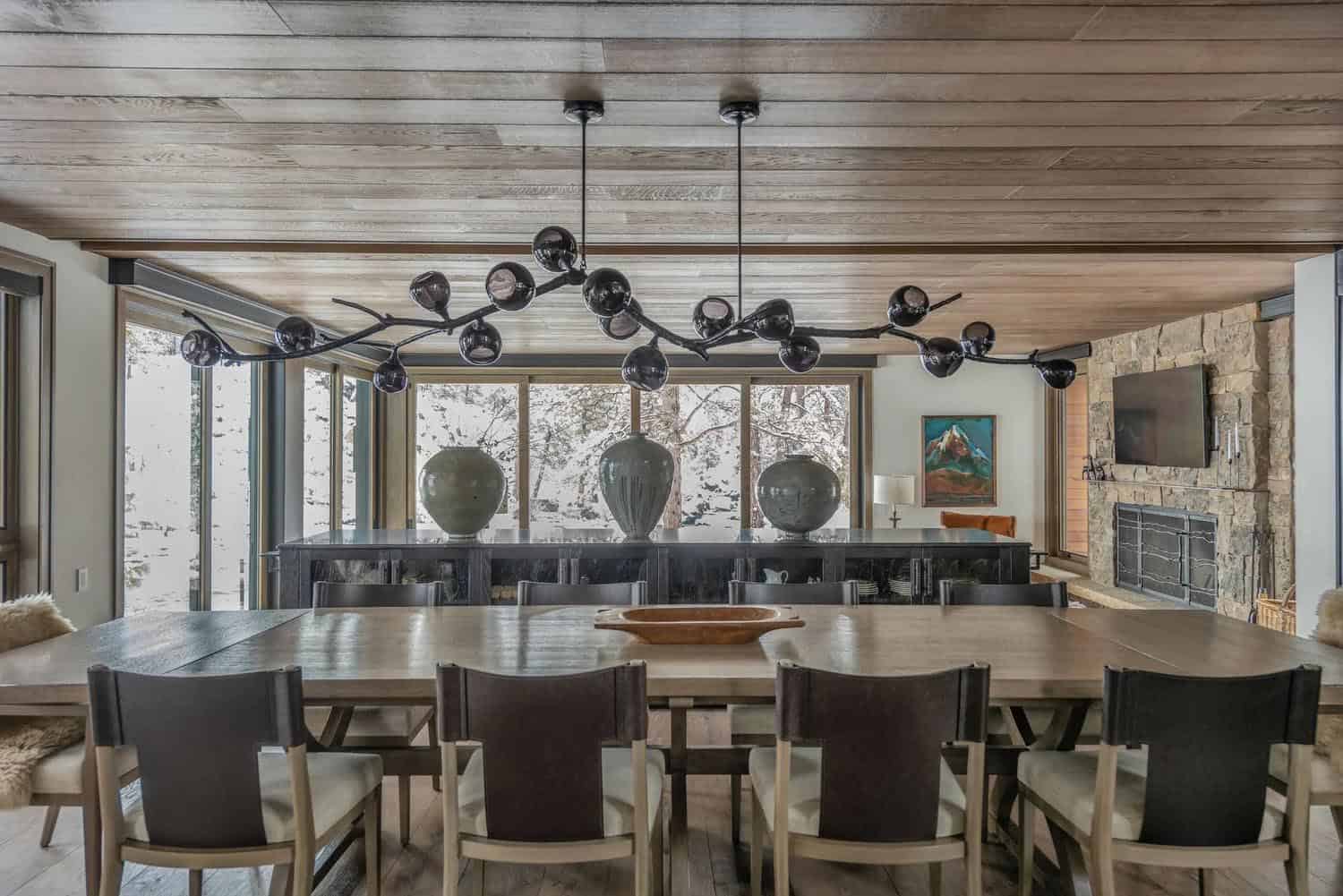 Large dining room with branch-style chandelier, wood dining table, and snowy forest views through sliding doors