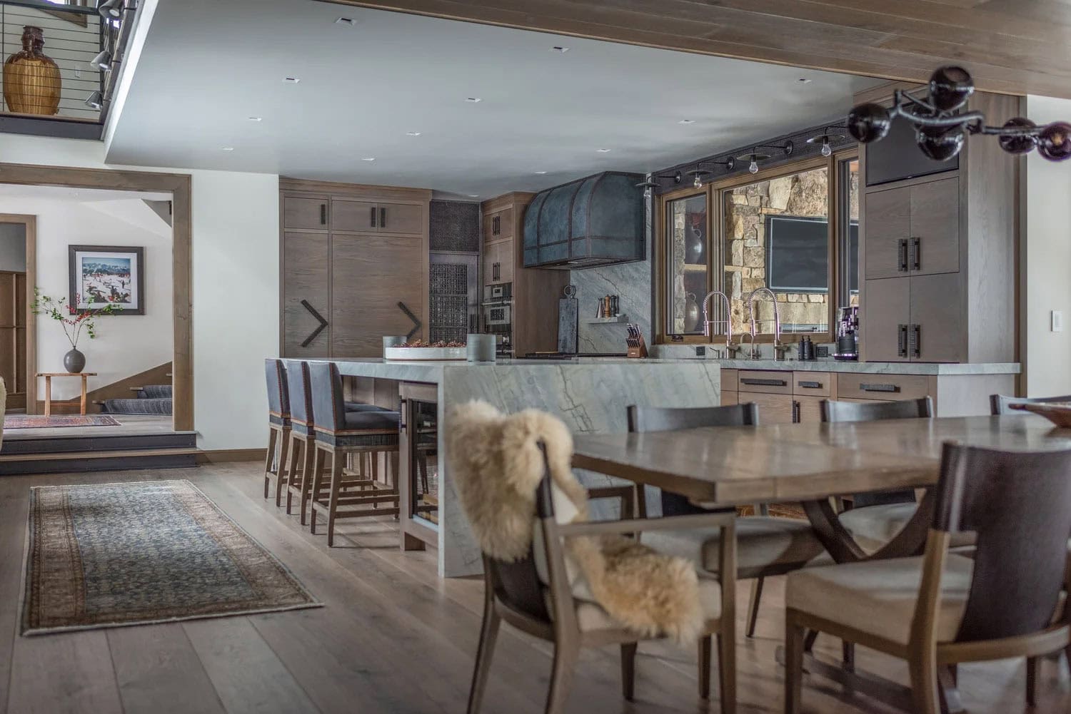 Open-plan kitchen and dining area with marble island, bar seating, sheepskin throws, and vintage runner rug