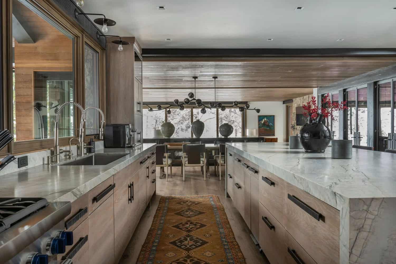 Long kitchen with dual marble countertops, professional range, globe pendants, and dining area beyond