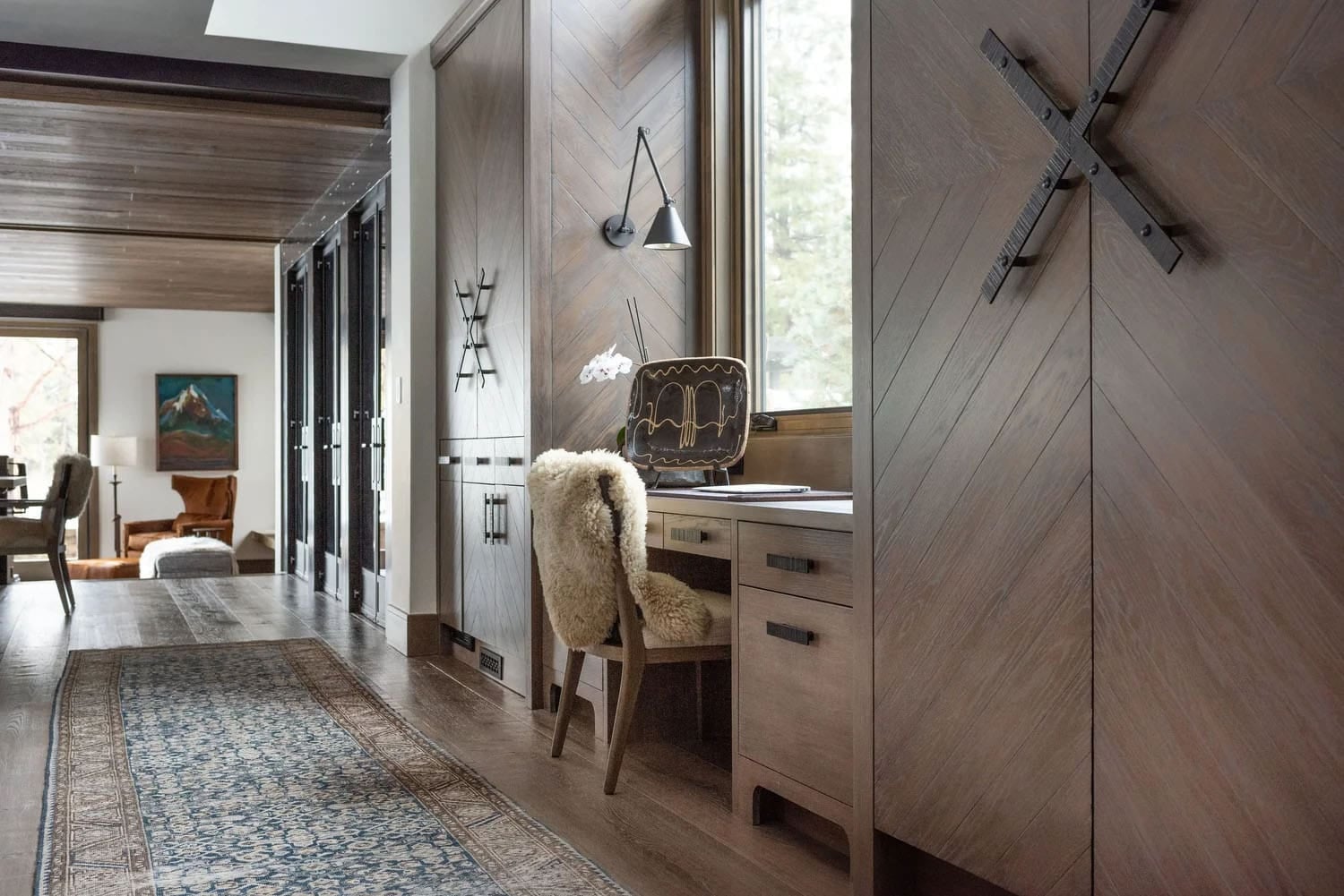 Hallway with built-in desk, herringbone wood cabinetry, barn door hardware, and runner rug leading to living room