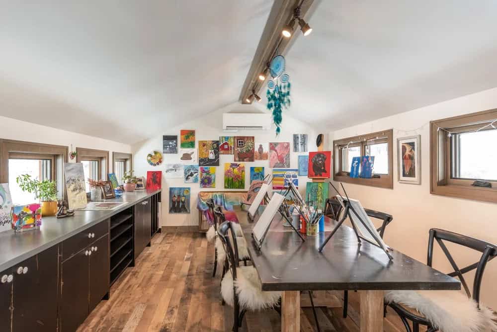 Colorful art studio with canvases covering the walls, easels at a long worktable, and track lighting