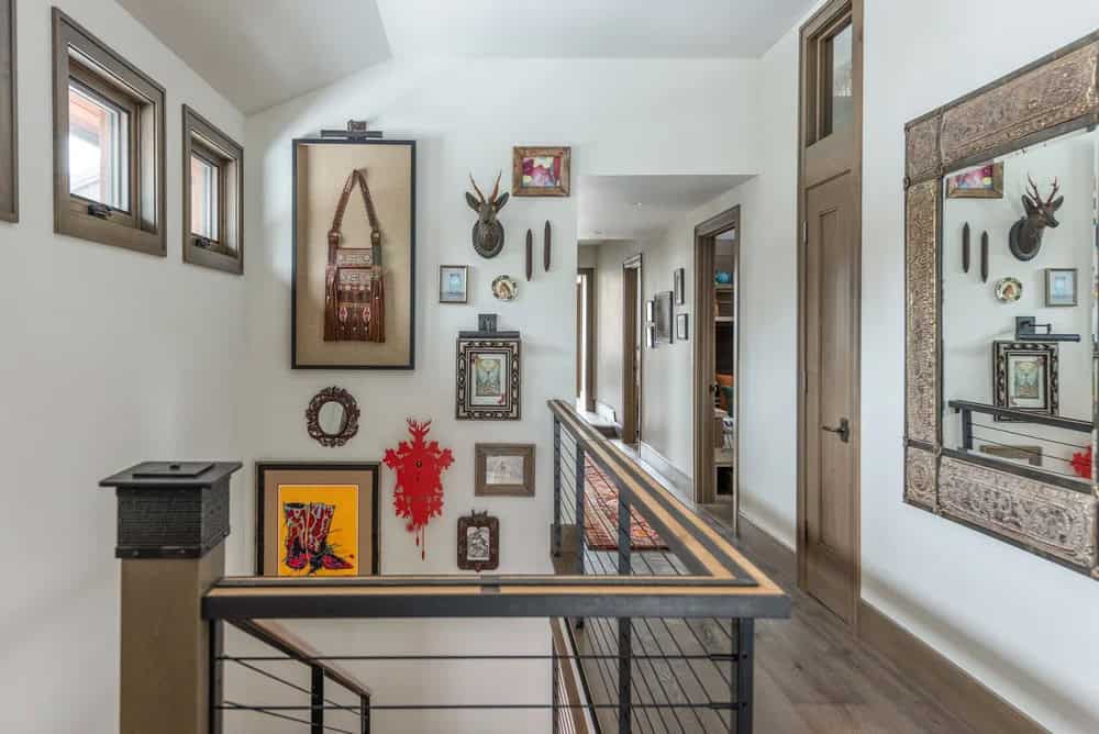 Upper hallway gallery wall with eclectic art, taxidermy, and decorative mirrors above cable railing