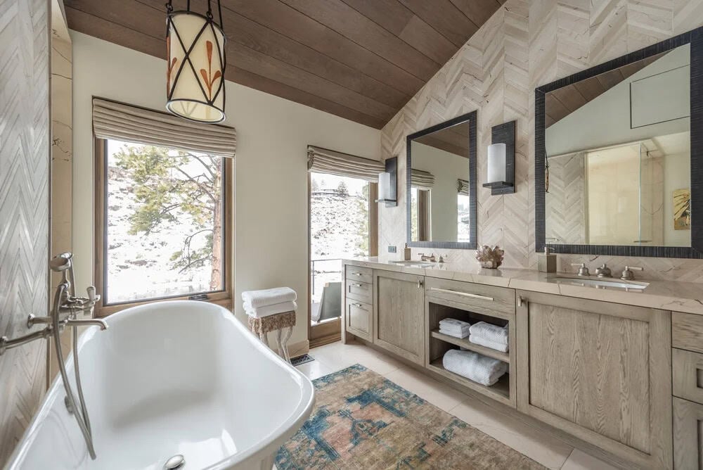 Primary bathroom with freestanding tub, herringbone tile wall, double vanity, and mountain views through windows