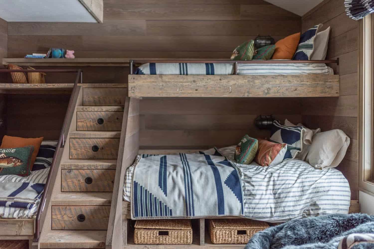 Detail of built-in wood bunk beds with drawer stairs, striped bedding, and woven storage baskets below