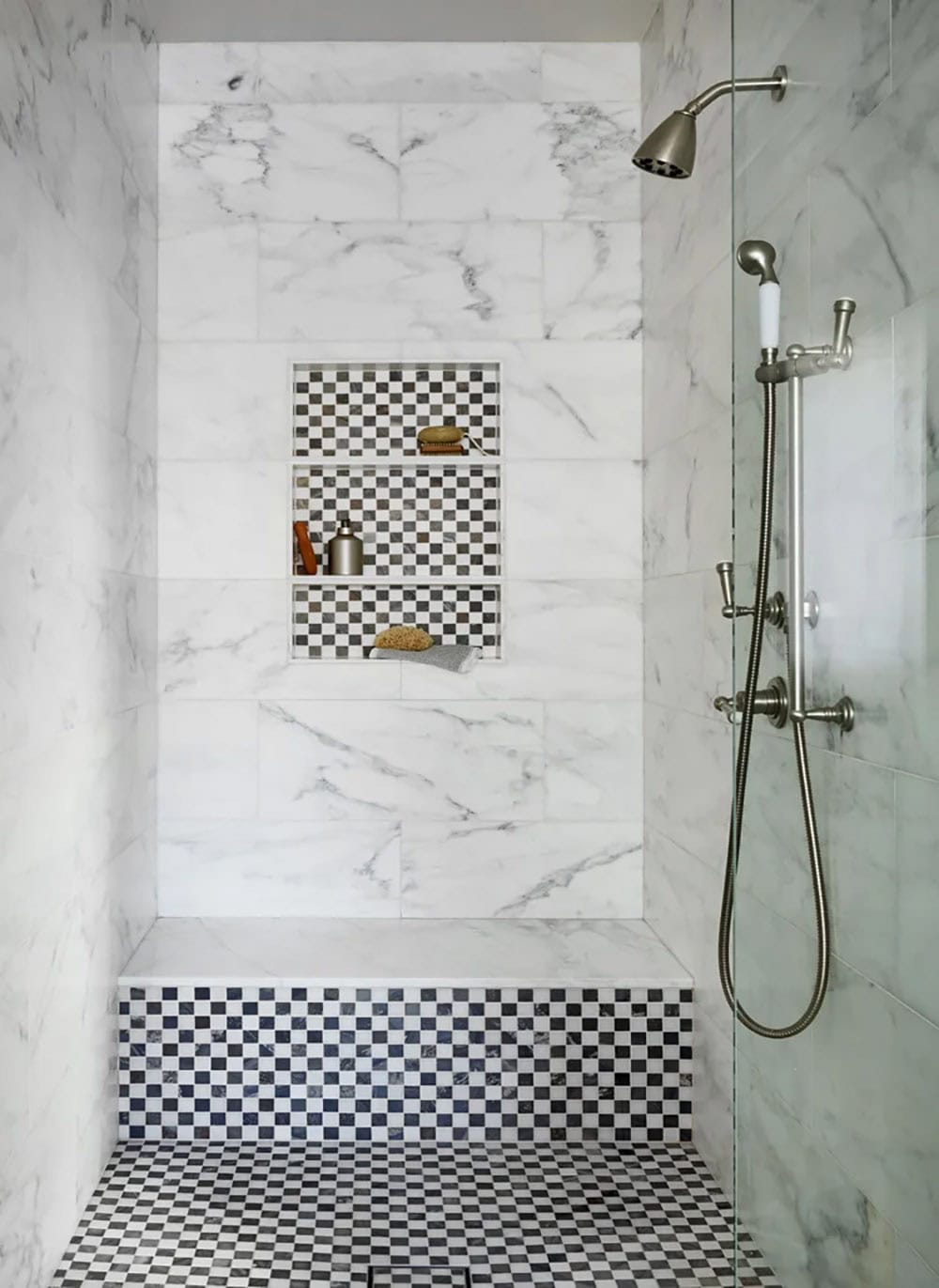 Marble-tiled walk-in shower with checkerboard mosaic floor, built-in niches, and brushed nickel fixtures