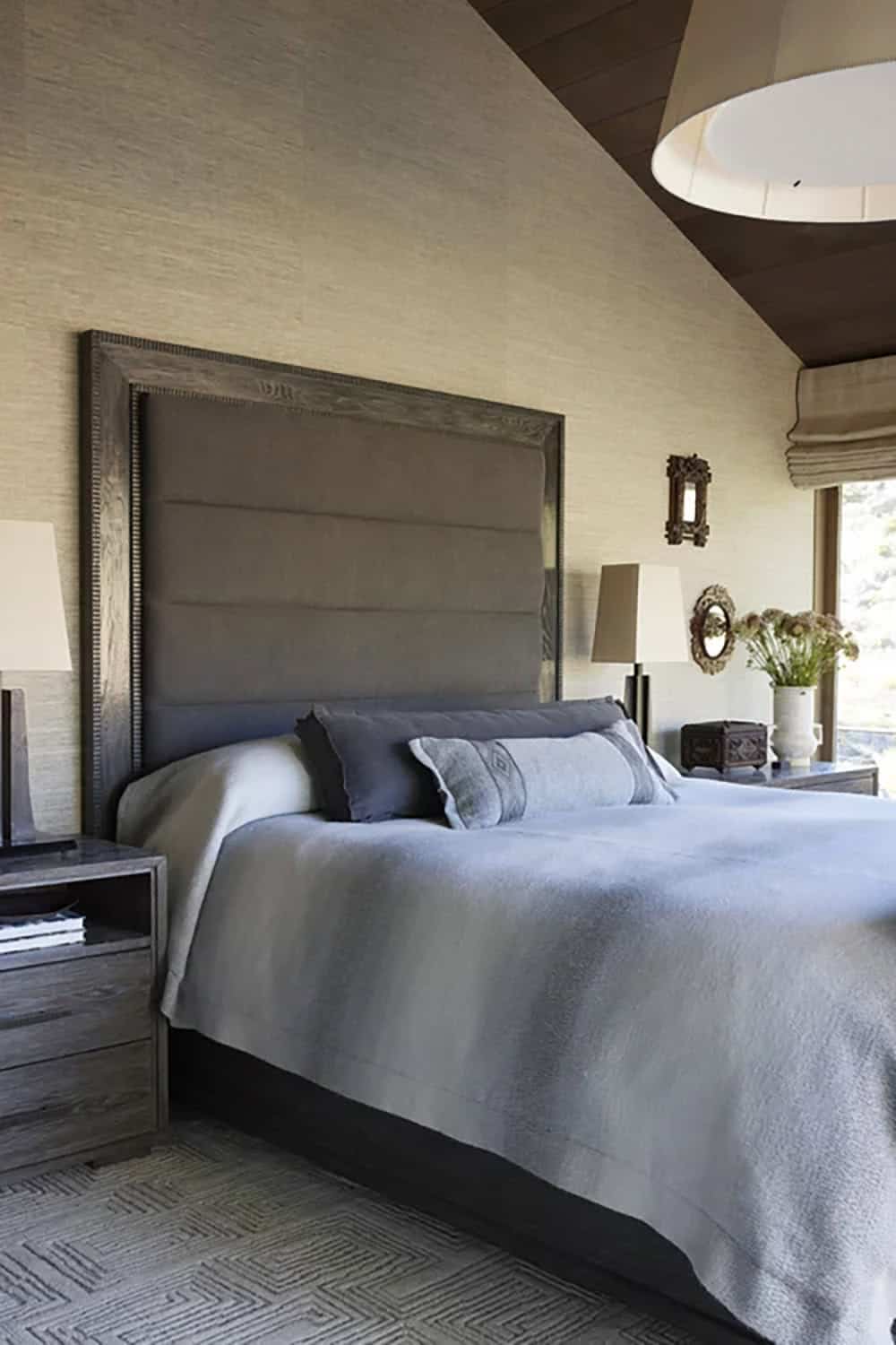 Primary bedroom with tall upholstered headboard, grasscloth wallpaper, gray bedding, and wood ceiling