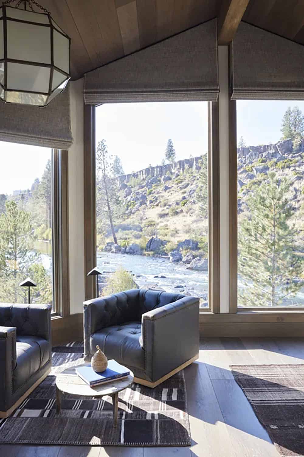 Sitting area with tufted leather chairs overlooking rocky river canyon through large picture windows