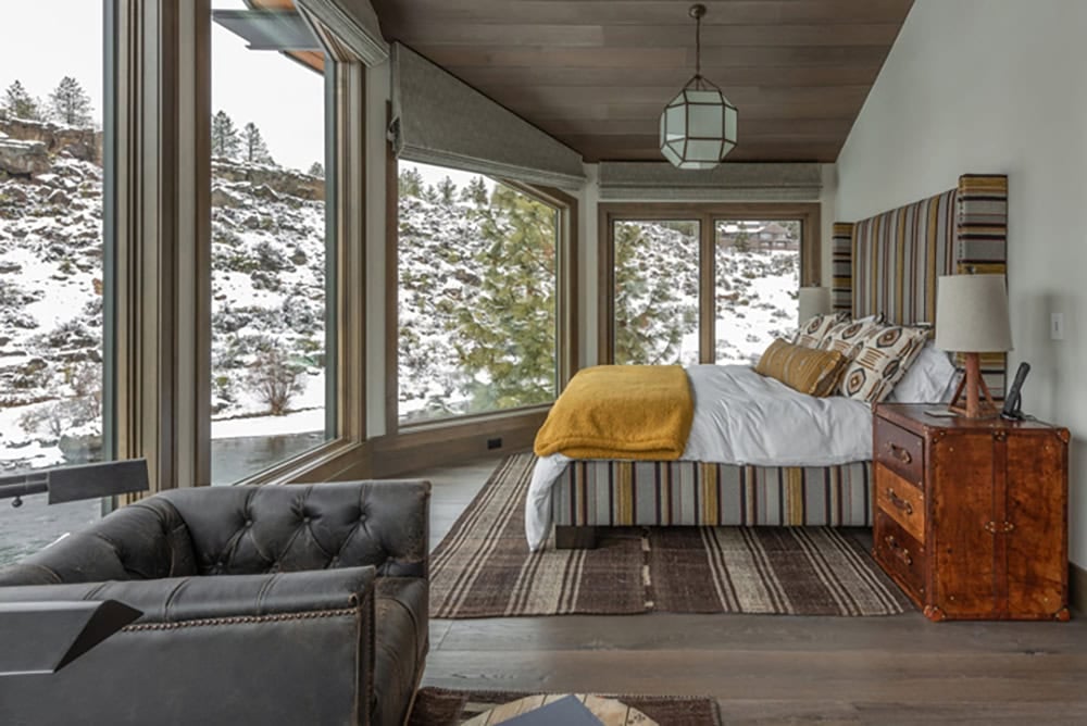 Guest bedroom with striped headboard, mustard throw, tufted leather chair, and panoramic snowy canyon views