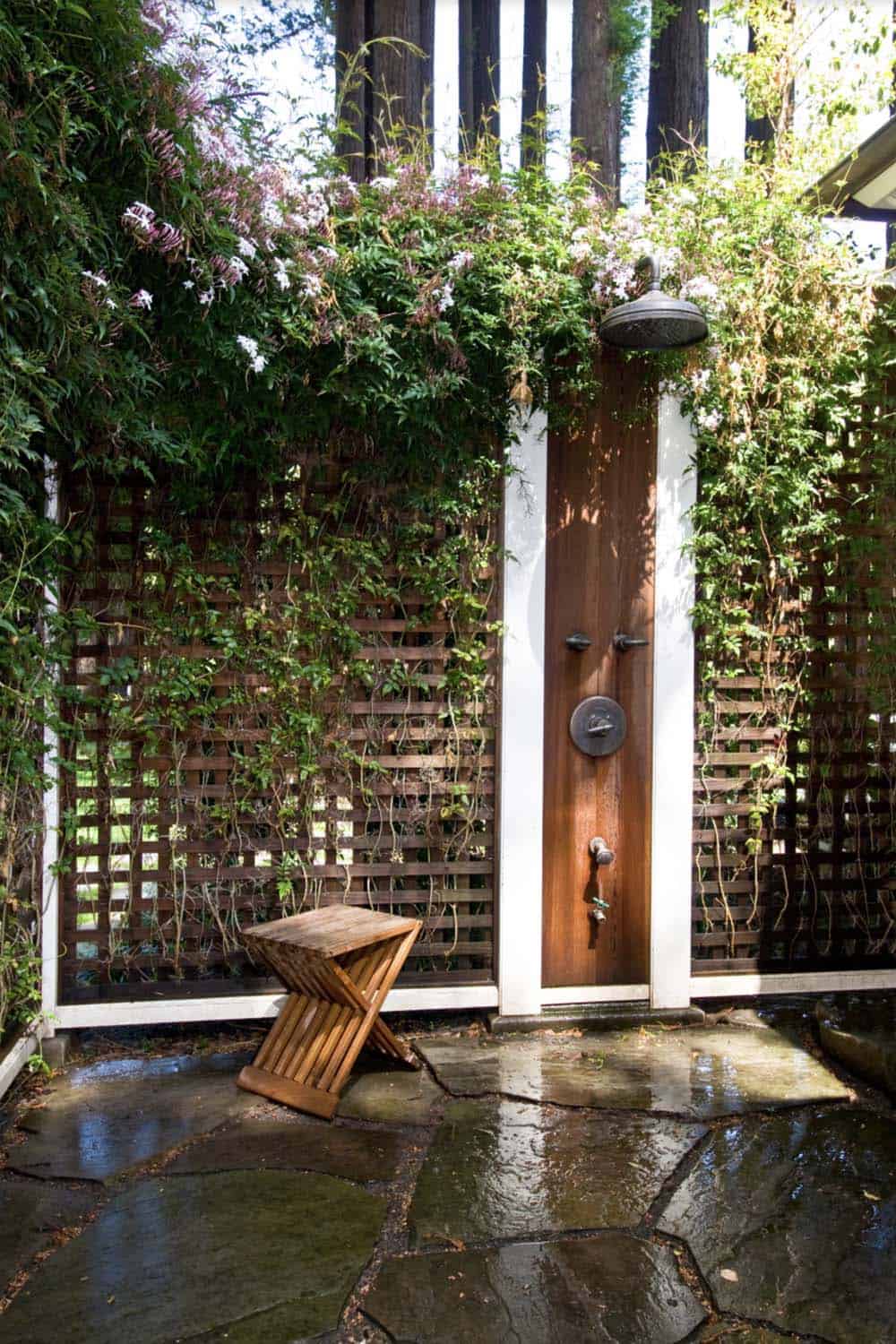 Outdoor shower with lattice trellis covered in flowering vines on a flagstone floor