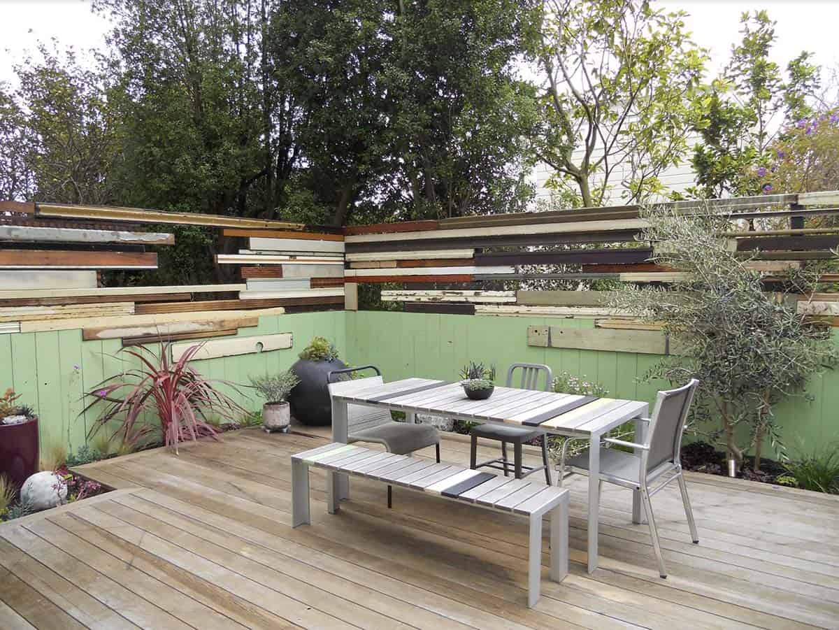 Eclectic reclaimed wood privacy fence above green painted wall on a wooden deck patio