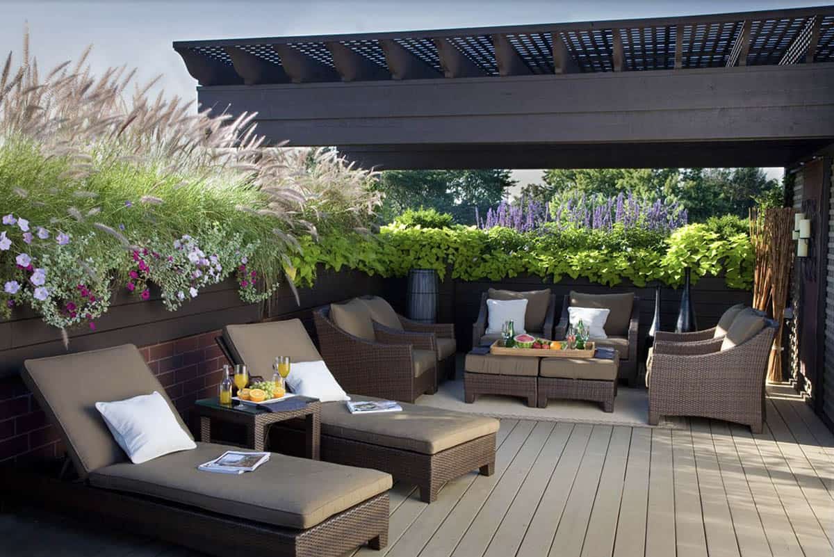 Rooftop deck with dark pergola, wicker lounge furniture, and a lush planter border of ornamental grasses, petunias, sweet potato vines, and purple salvia for privacy