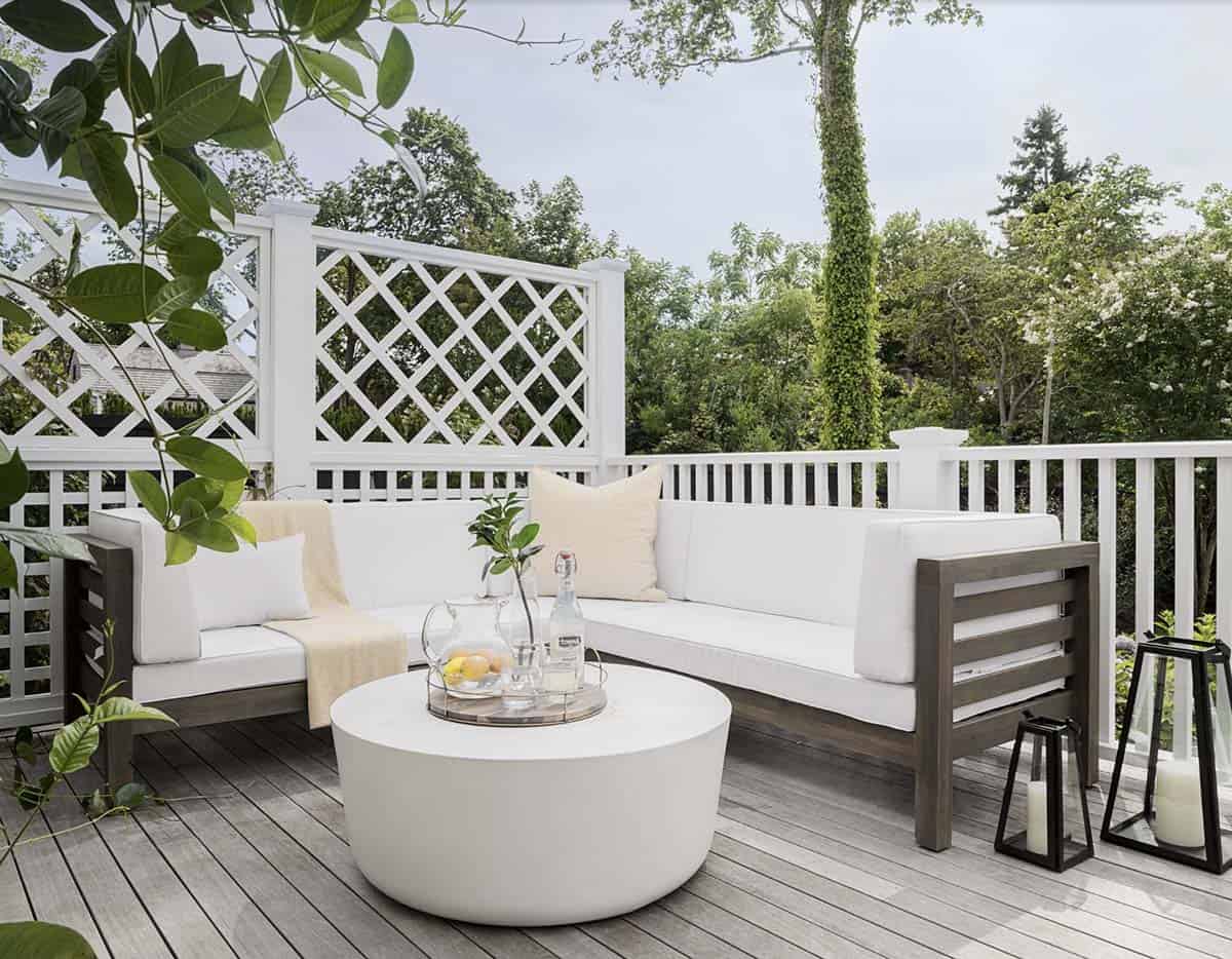White lattice privacy screen on a deck with grey wood outdoor sofa, round white concrete coffee table, and floor lanterns