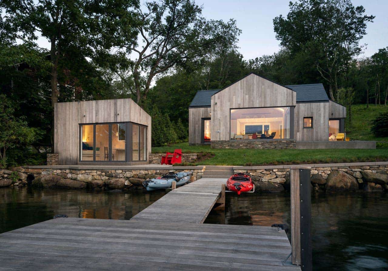 Prefab cross-laminated timber lake house in Connecticut viewed from the dock at dusk, with kayaks in the foreground