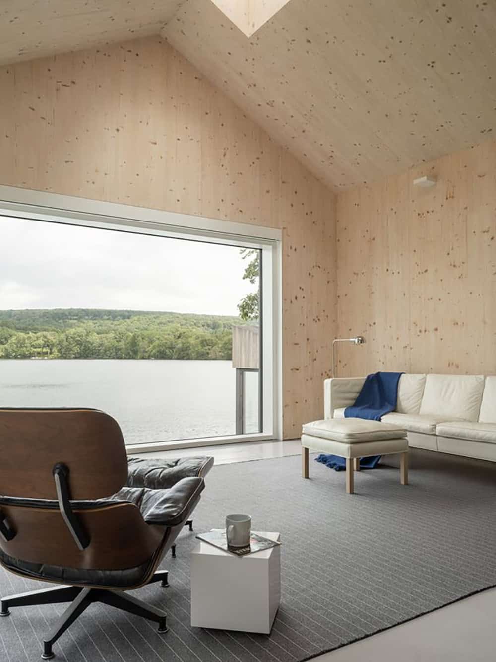 Cross-laminated timber living room with white sofa, Eames lounge chair, and panoramic lake view