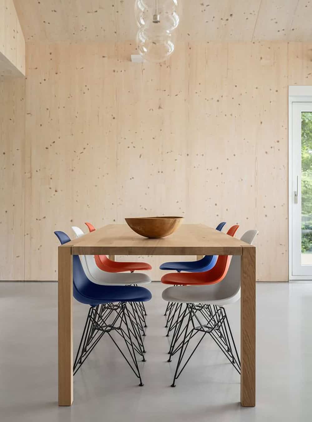 Dining table with multicolored Eames shell chairs against CLT wall panels