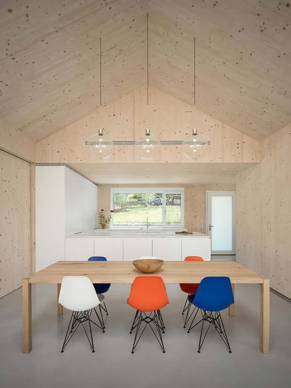 Dining area with Eames chairs and white kitchen in a CLT-paneled gable-roofed room
