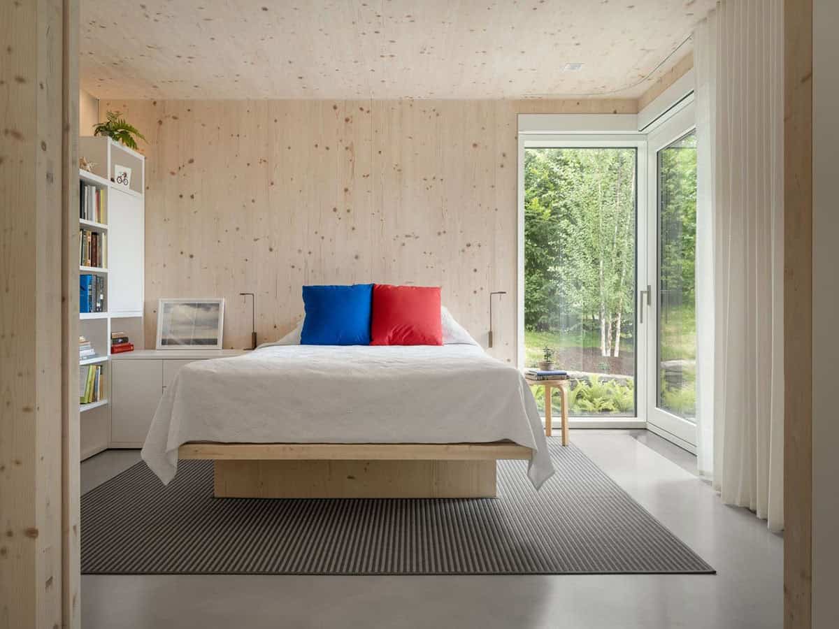 CLT bedroom with platform bed, red and blue pillows, built-in shelving, and garden views